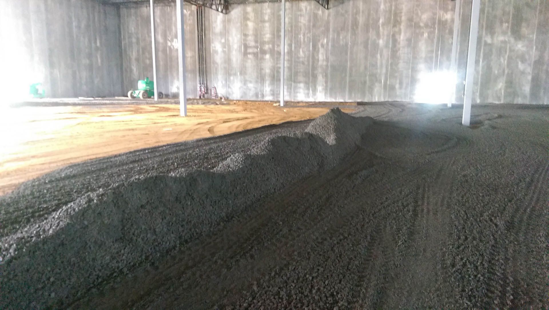 Gray concrete floor with piles of dark material inside a building, possibly construction site.