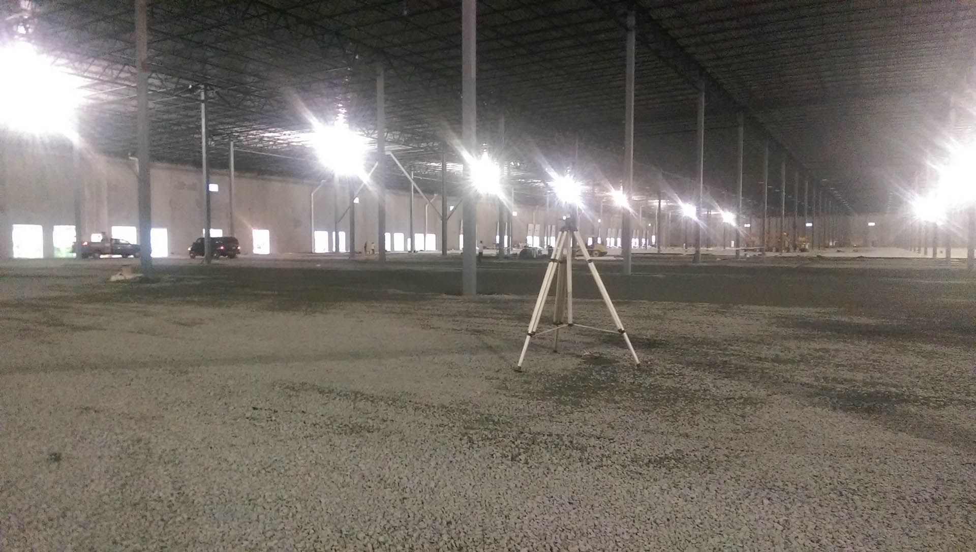 Large, empty warehouse interior with bright overhead lights and a surveying instrument.