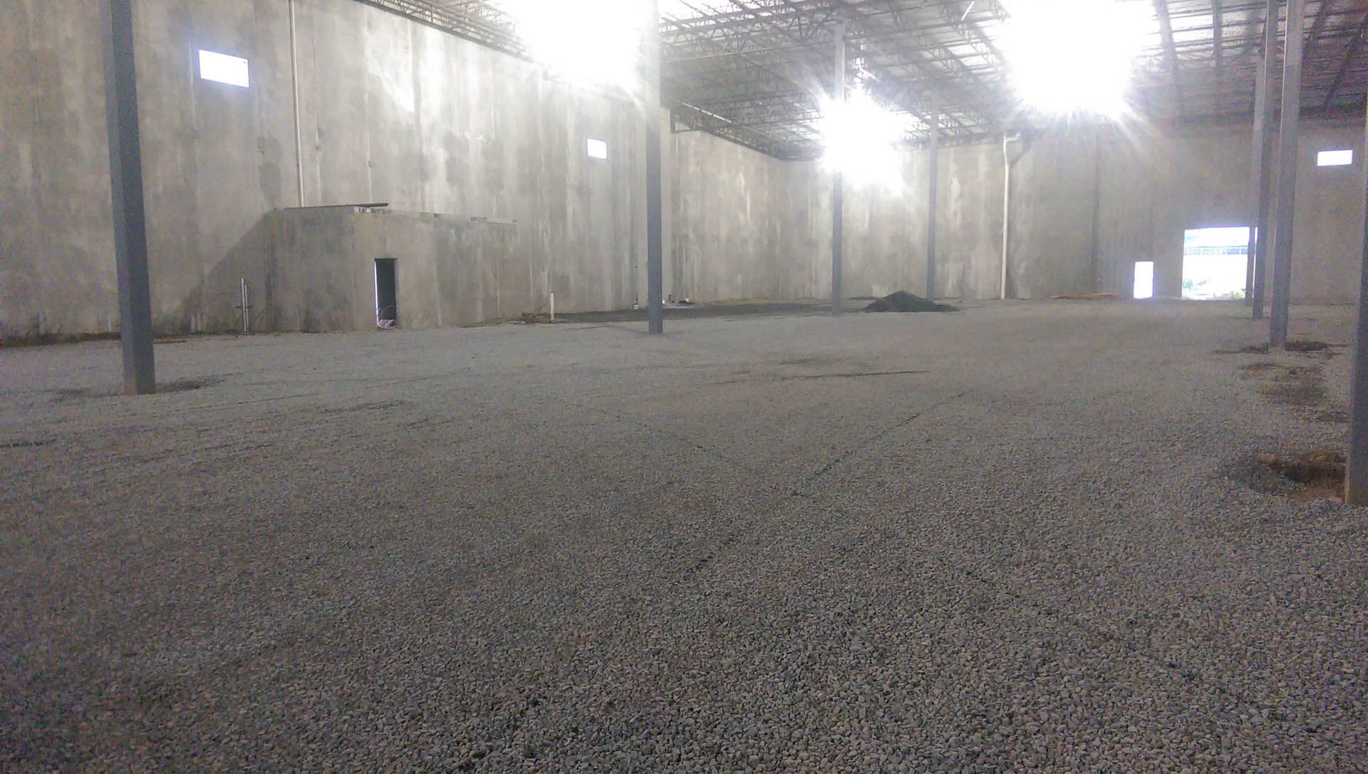 Empty industrial warehouse with gray gravel floor and concrete walls.