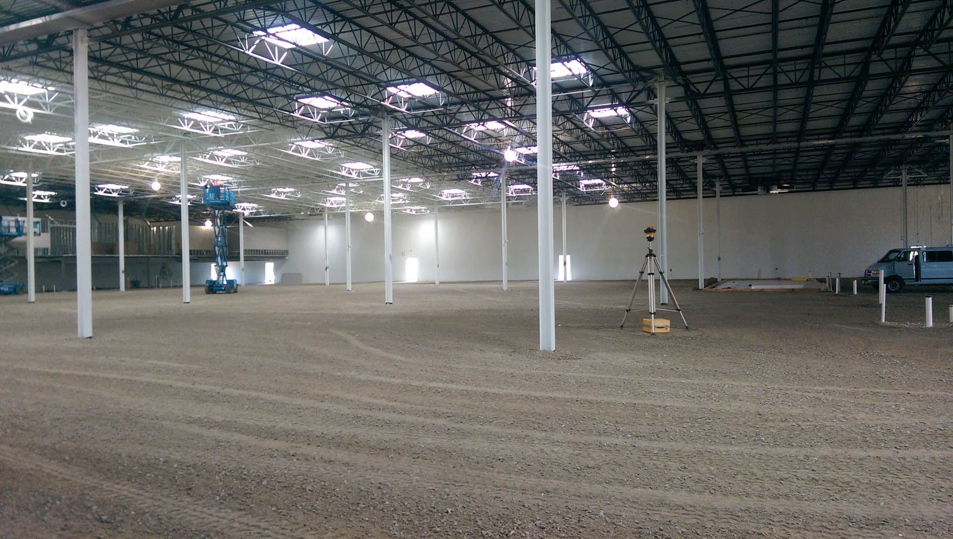 Large, empty indoor arena with sand floor, white supports, and metal roof.