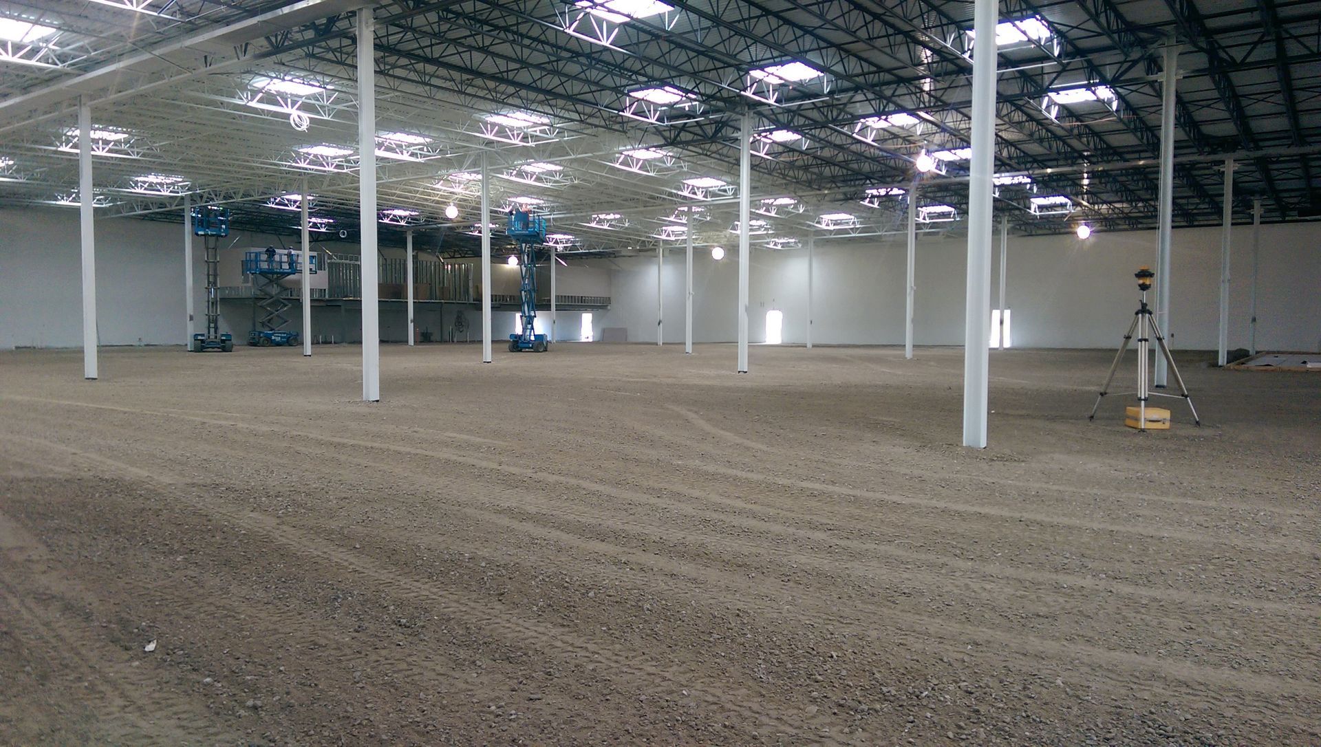 Large empty warehouse interior with gravel floor, support columns, and overhead lighting.