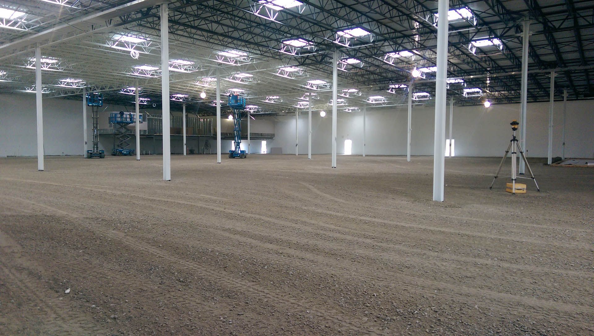 An empty warehouse interior with a dirt floor, white pillars, and a metal ceiling.