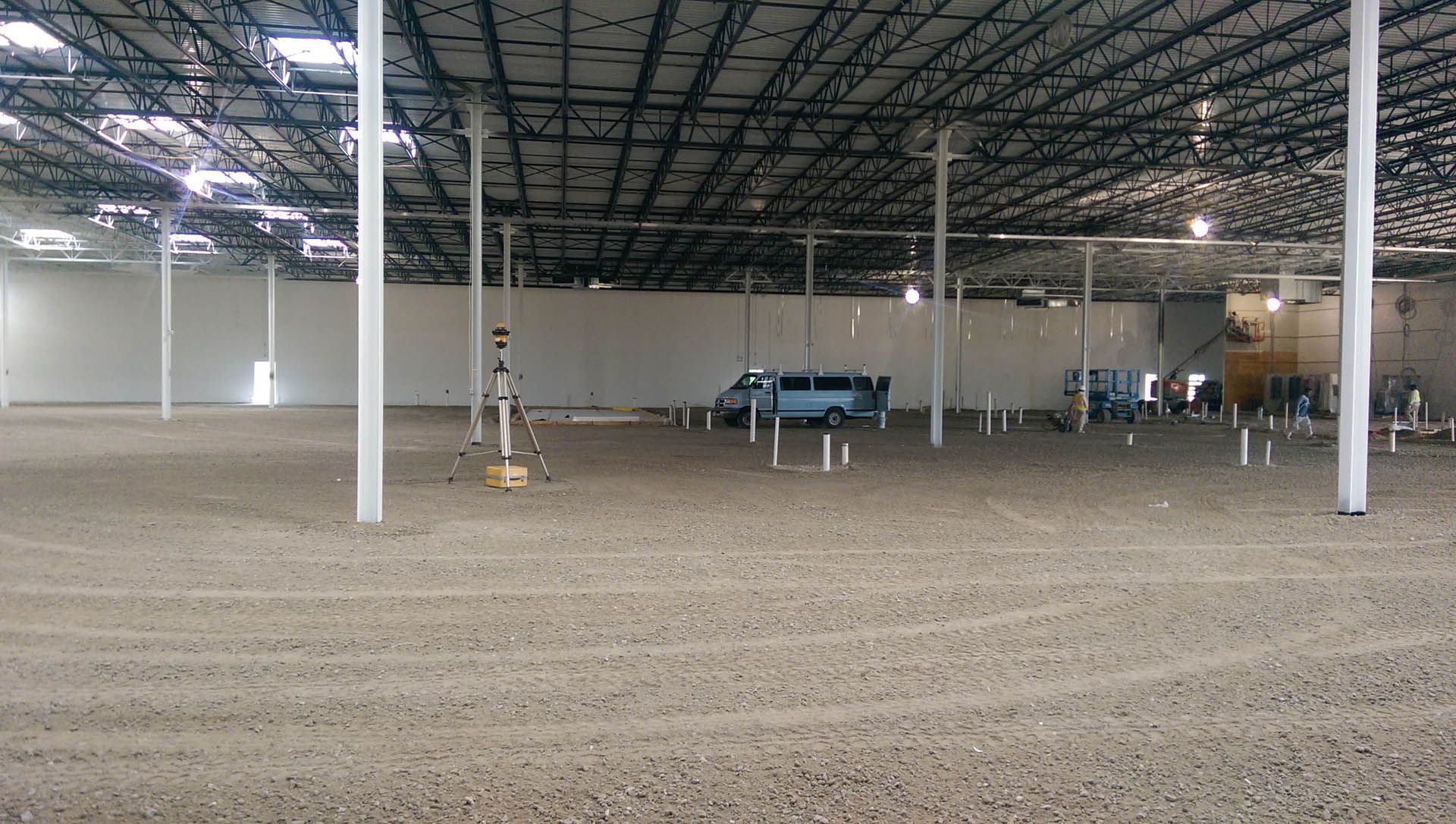 Indoor equestrian arena with dirt floor, white support beams, and a blue van.