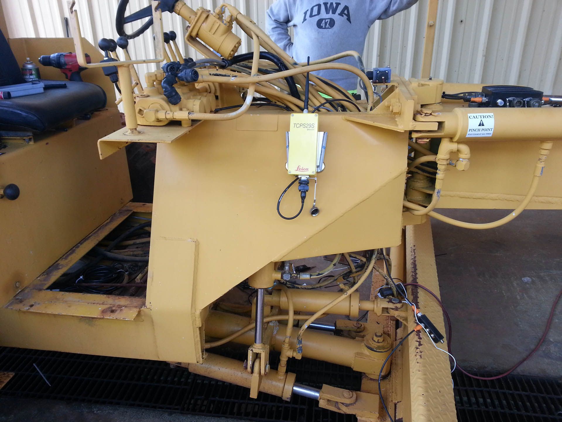 Yellow grader with attached device, person in background.