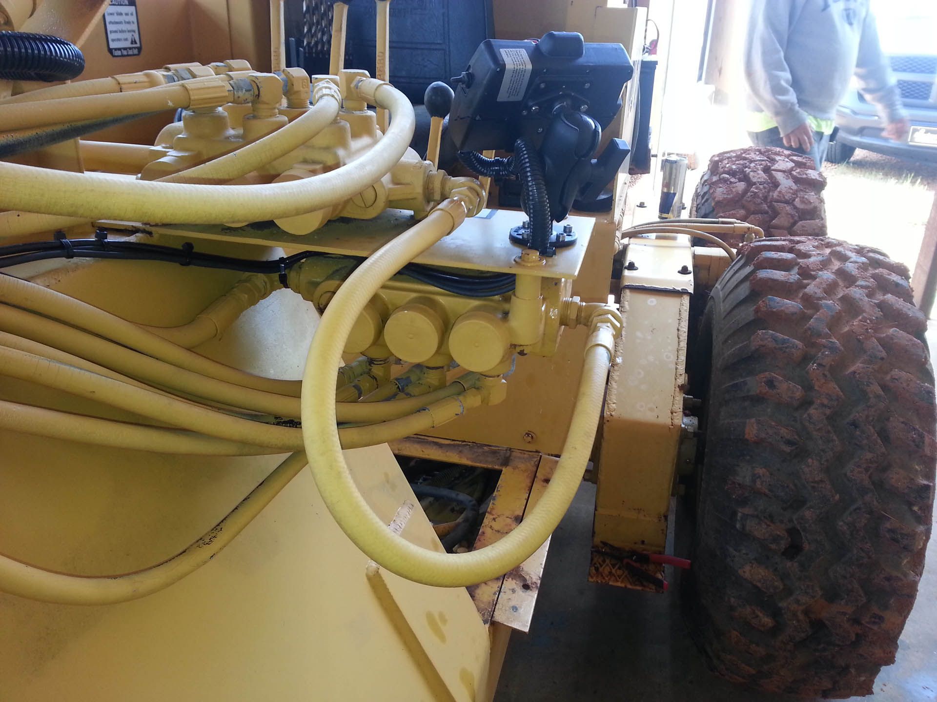 Yellow construction vehicle with large tires, hoses, and control levers, likely outdoors.