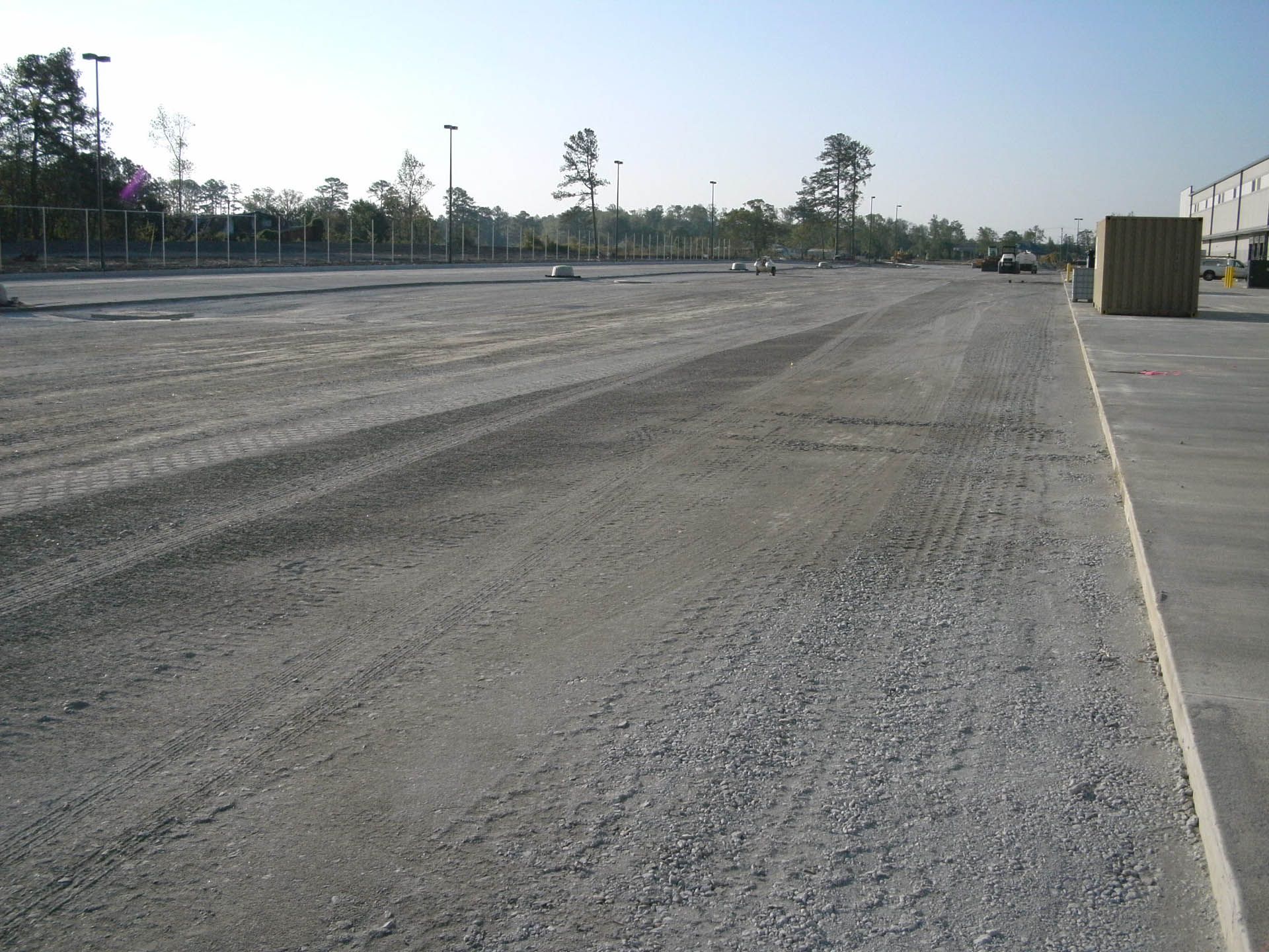Gravel lot, possibly for a warehouse. Gray gravel surface, industrial setting, empty.