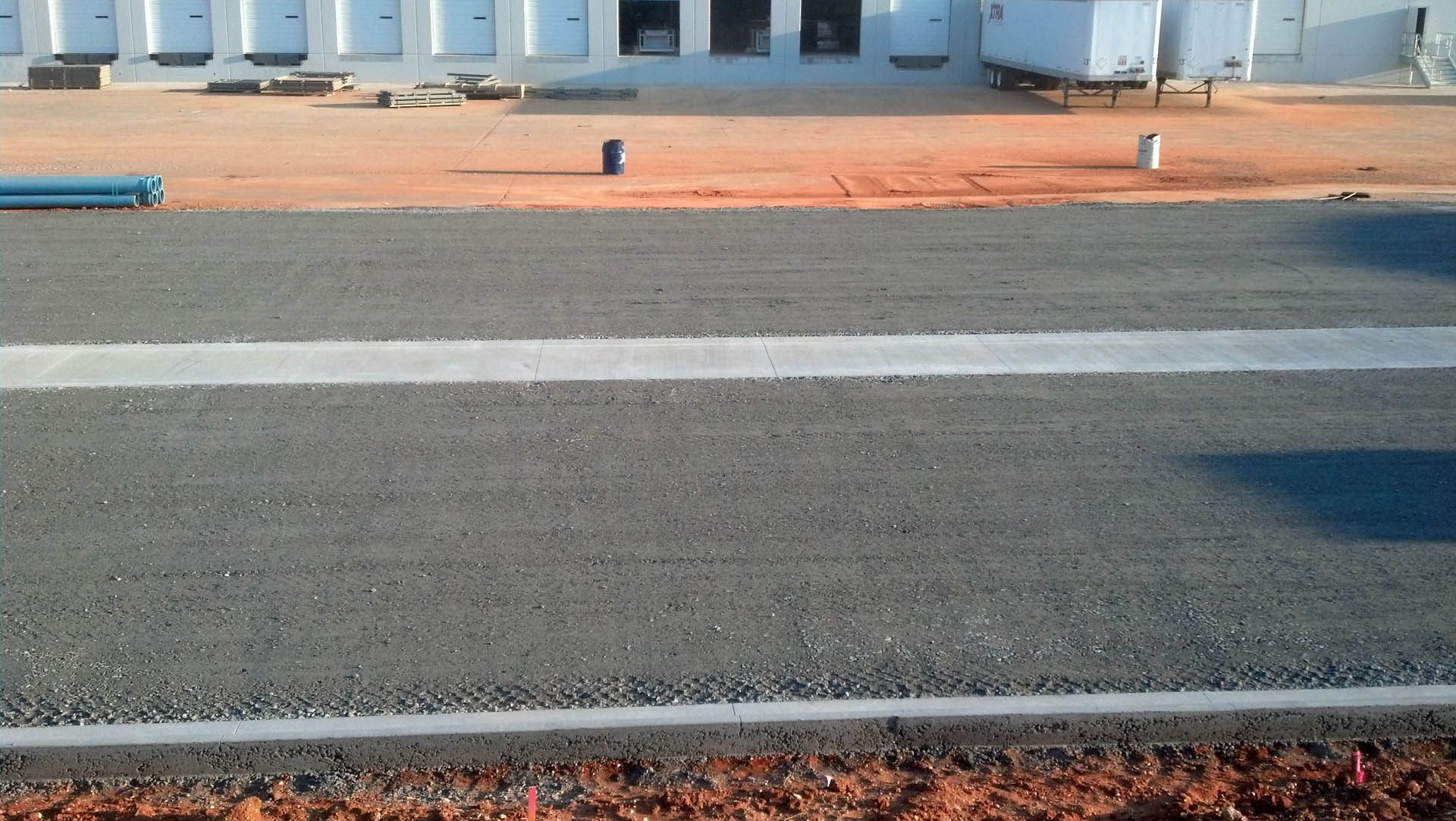 Asphalt road with white line in front of a building with loading docks; red dirt.