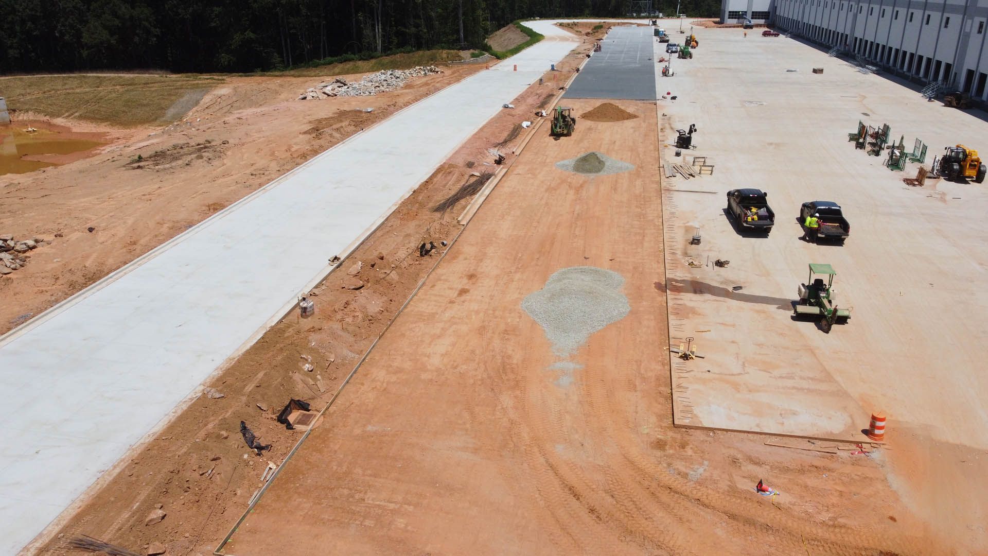 Aerial view of construction site with concrete pathway, machinery, and partially built warehouse.
