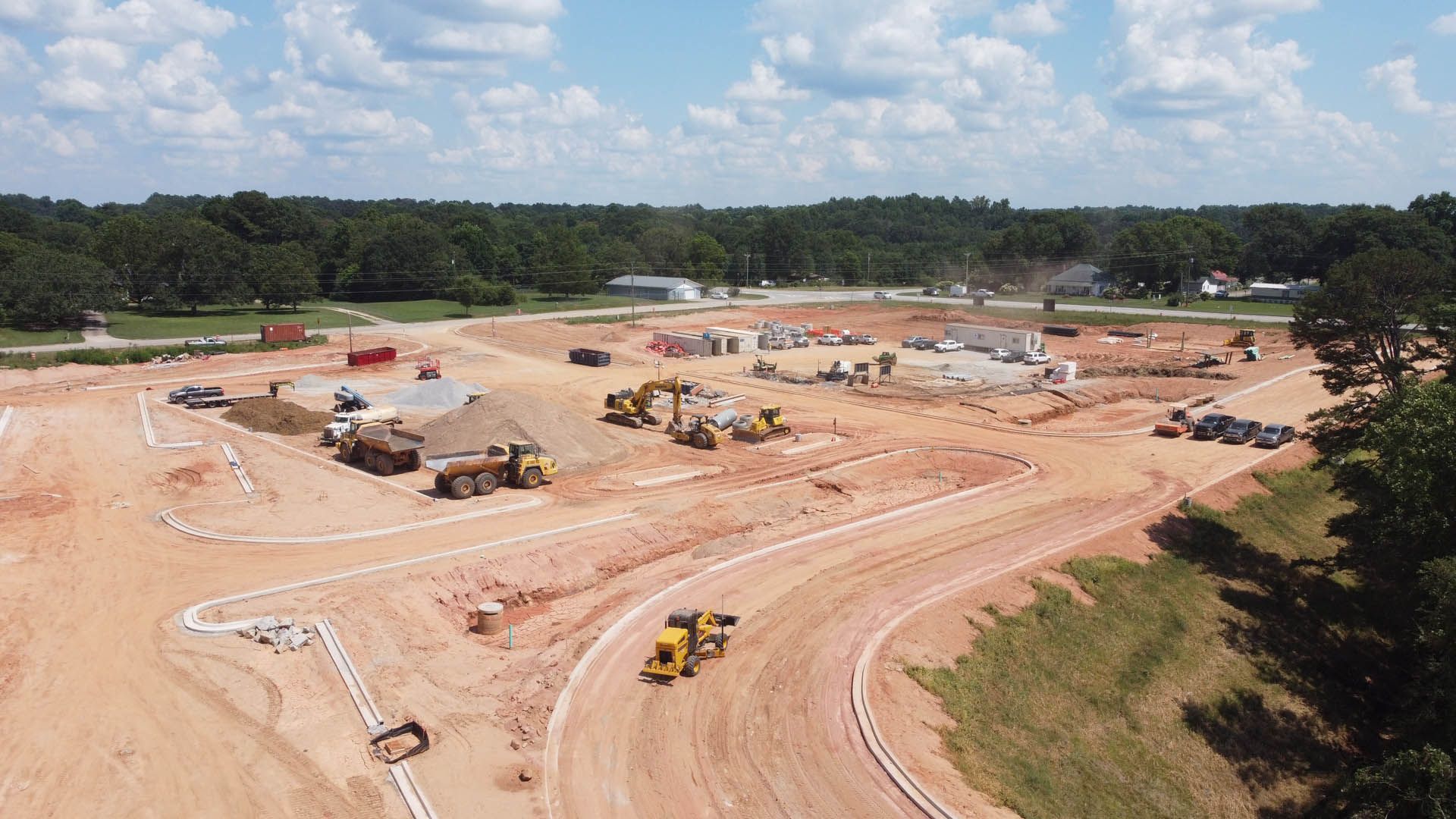 Construction site with earth-moving equipment, buildings under construction, and dirt roads under a blue sky.