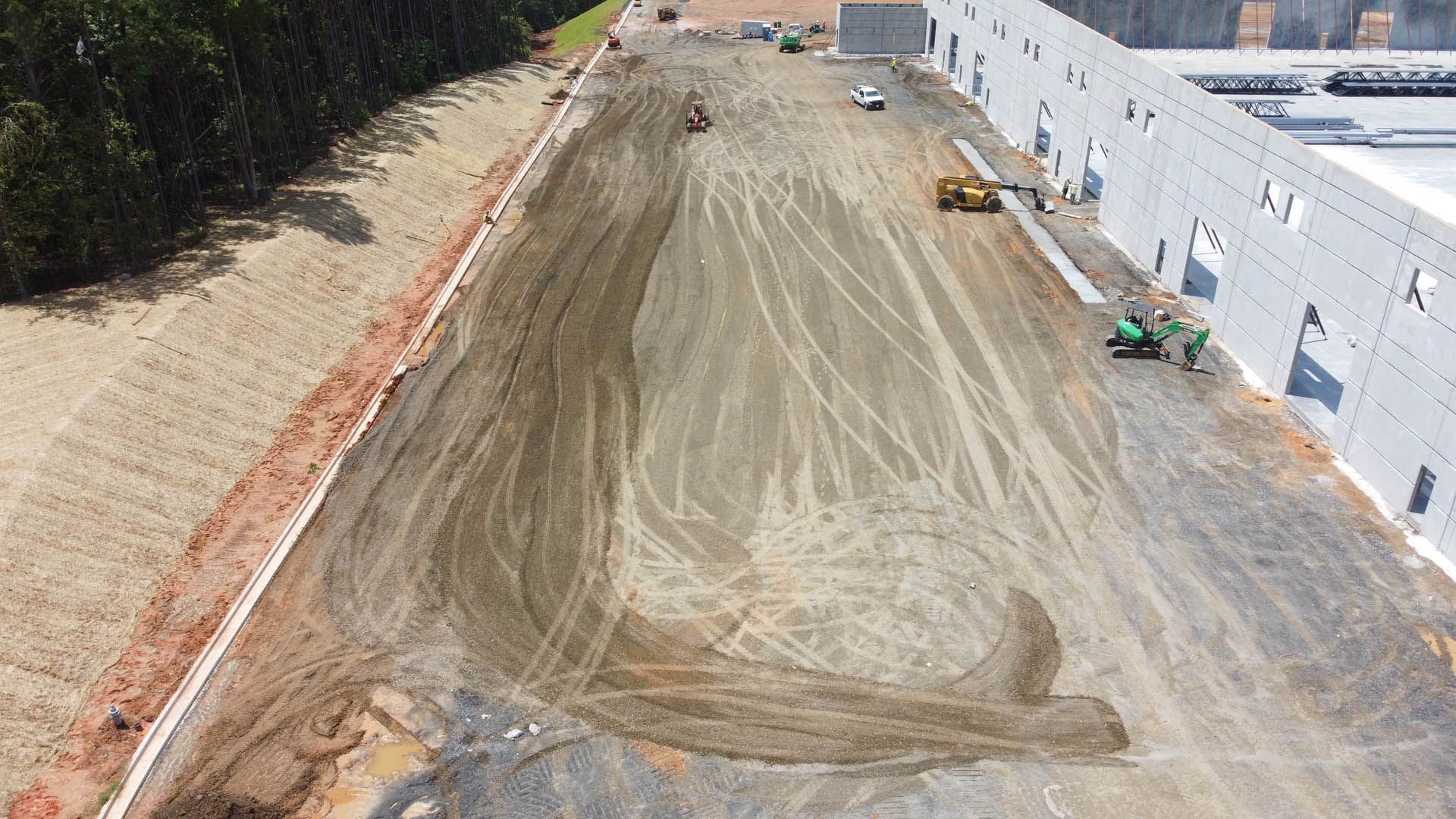 Construction site with earthmovers leveling a gravel area next to a large industrial building.