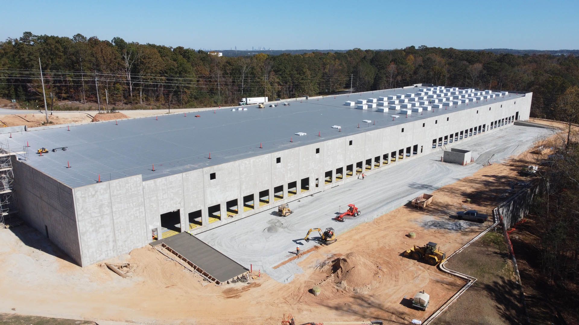 Large industrial warehouse under construction, concrete walls, loading docks, construction equipment, bright sunlight.
