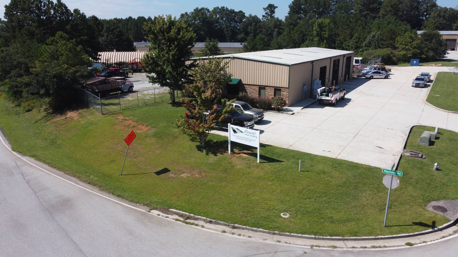 Aerial view of a business building with cars parked nearby, green grass, and a street corner.