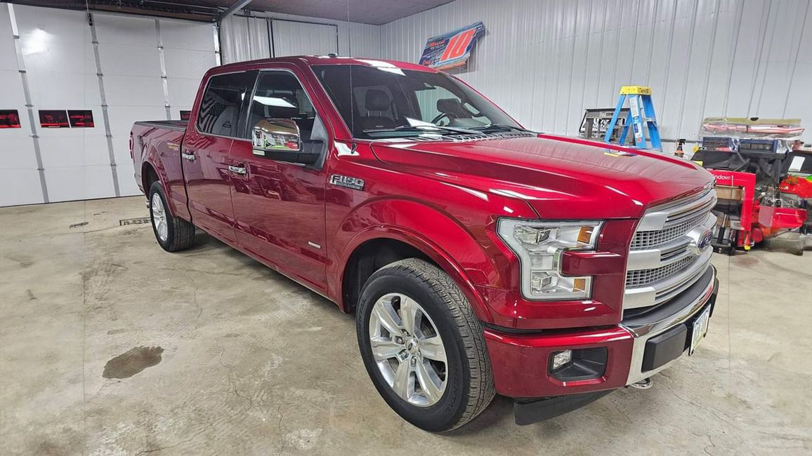 Red pickup truck parked inside a garage or auto shop, front three-quarter view.
