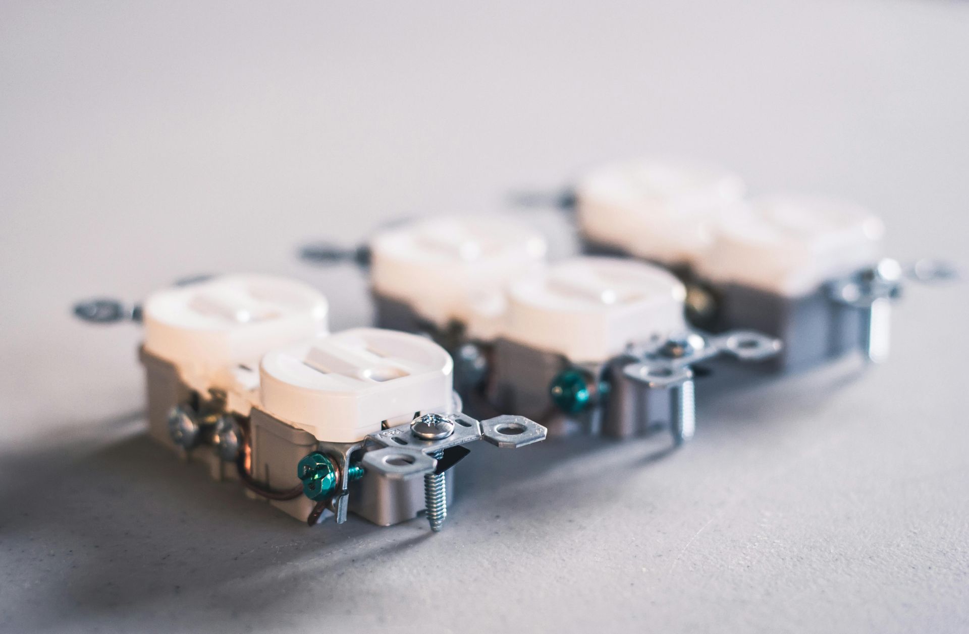 Three electrical outlets on a light-colored surface, close up. The outlets are white and gray.