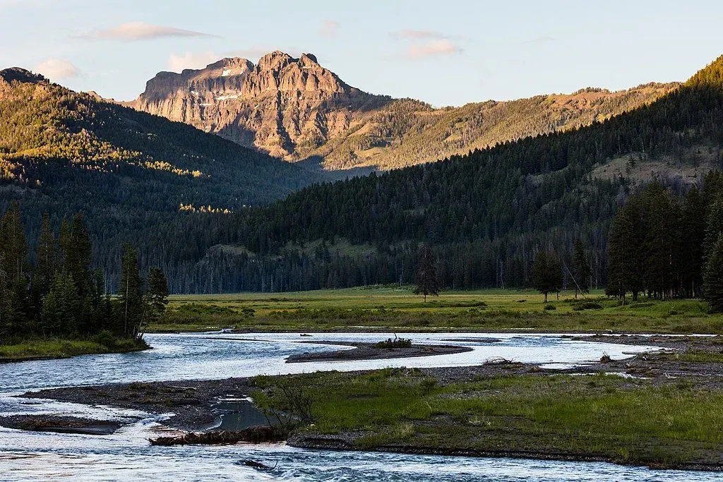 Mountain lake and forest under warm sunset light with rocky peaks in the background