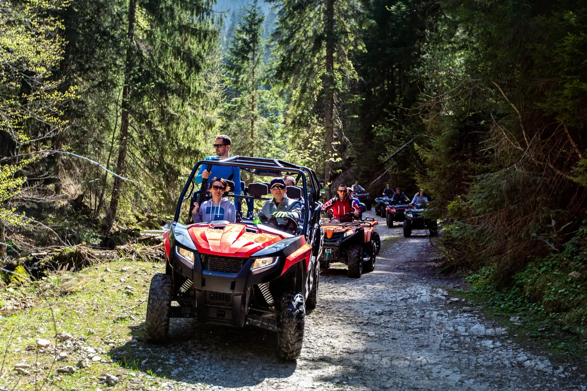 People riding red and blue off-road vehicles on a forest trail