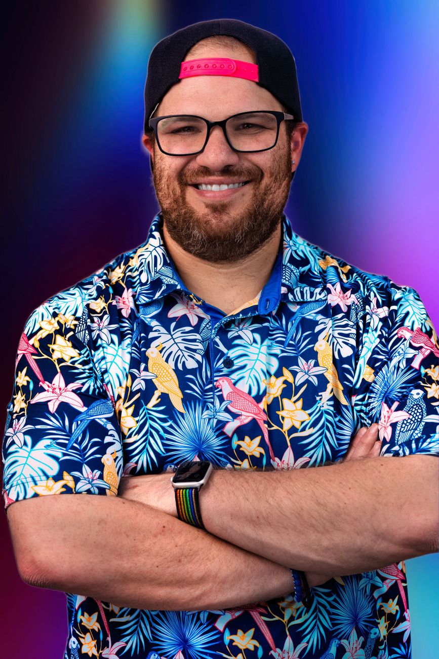 A man wearing glasses and a hat is standing with his arms crossed.