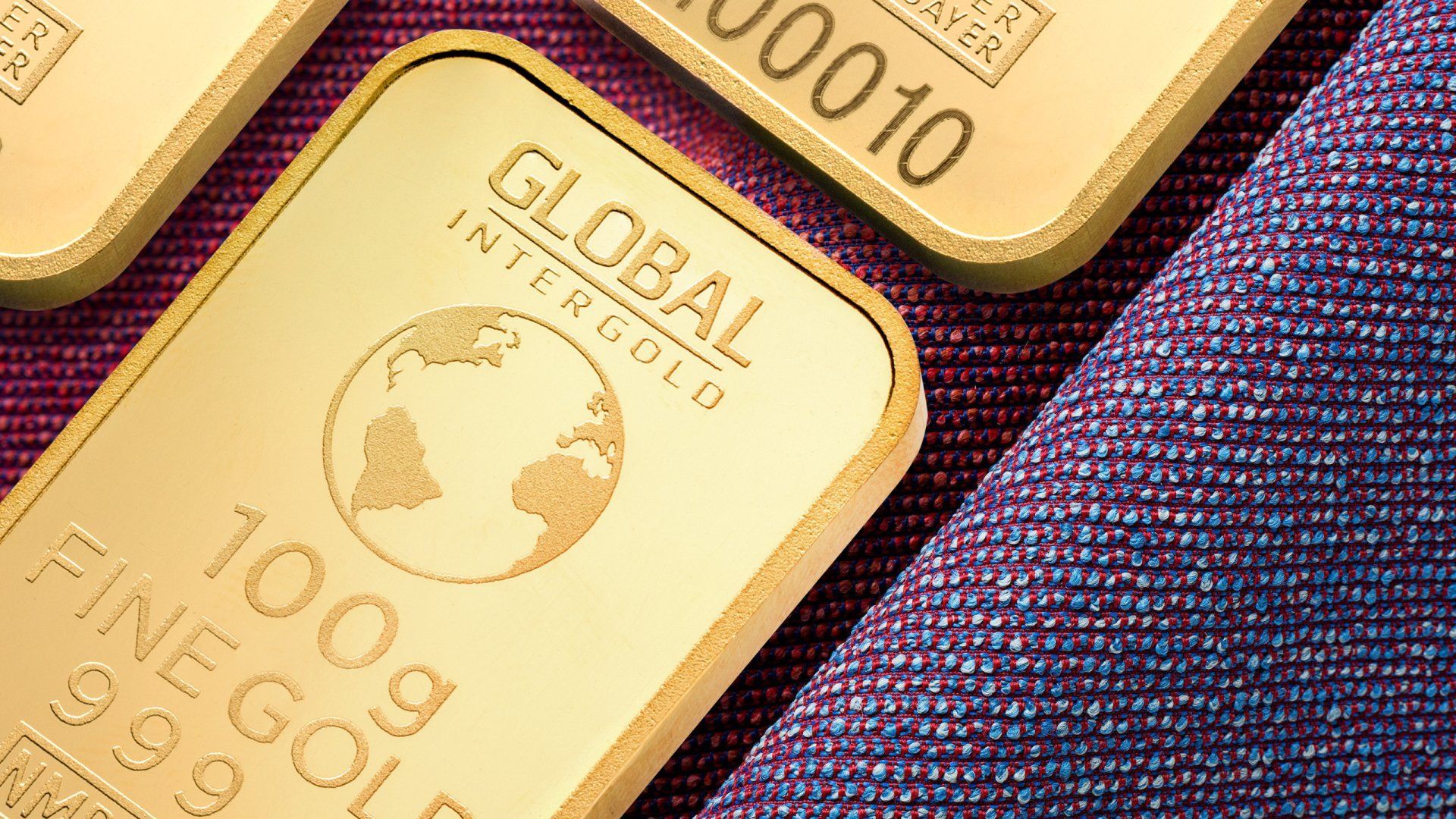 Three gold bars are sitting on top of a purple cloth.