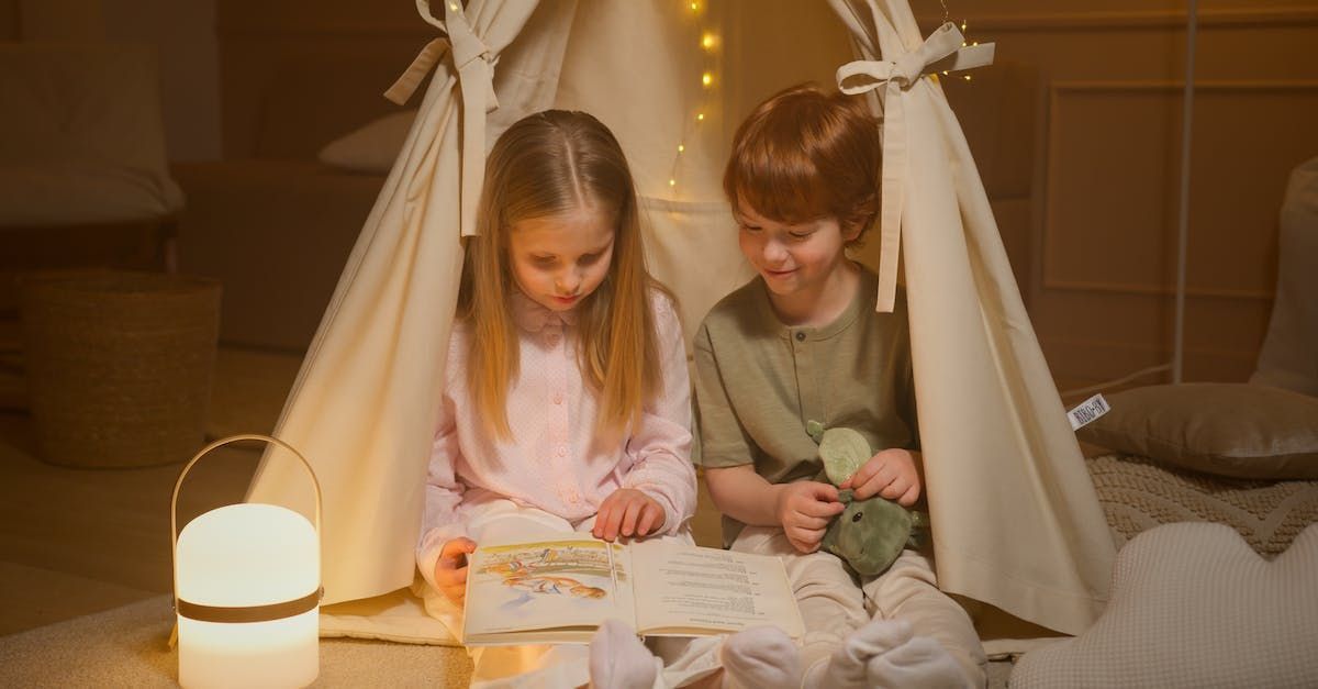A boy and a girl are sitting in a teepee reading a book.