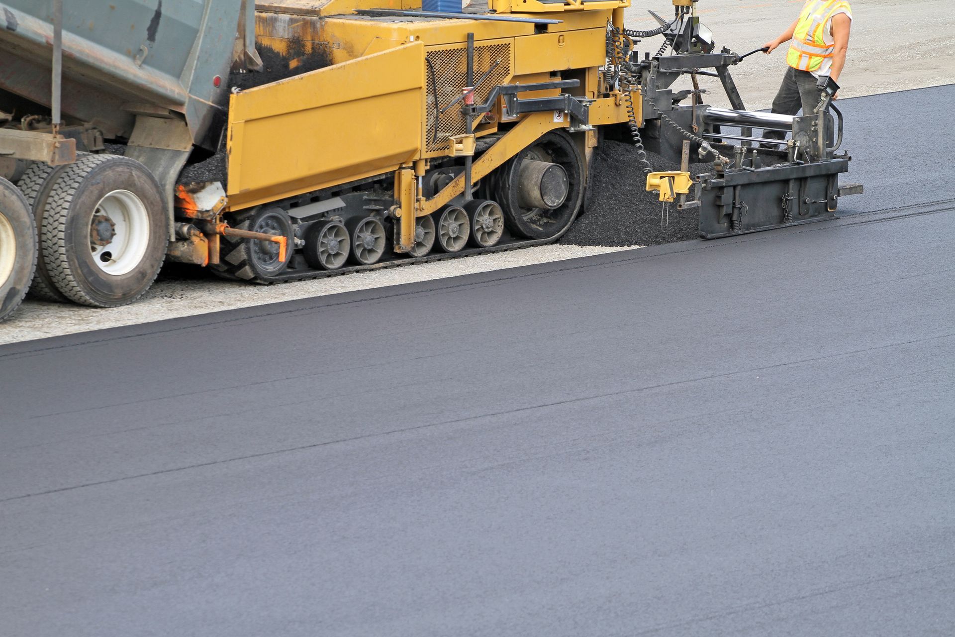Crop view of commercial asphalt paving contractors, working with a yellow machine on a parking lot.