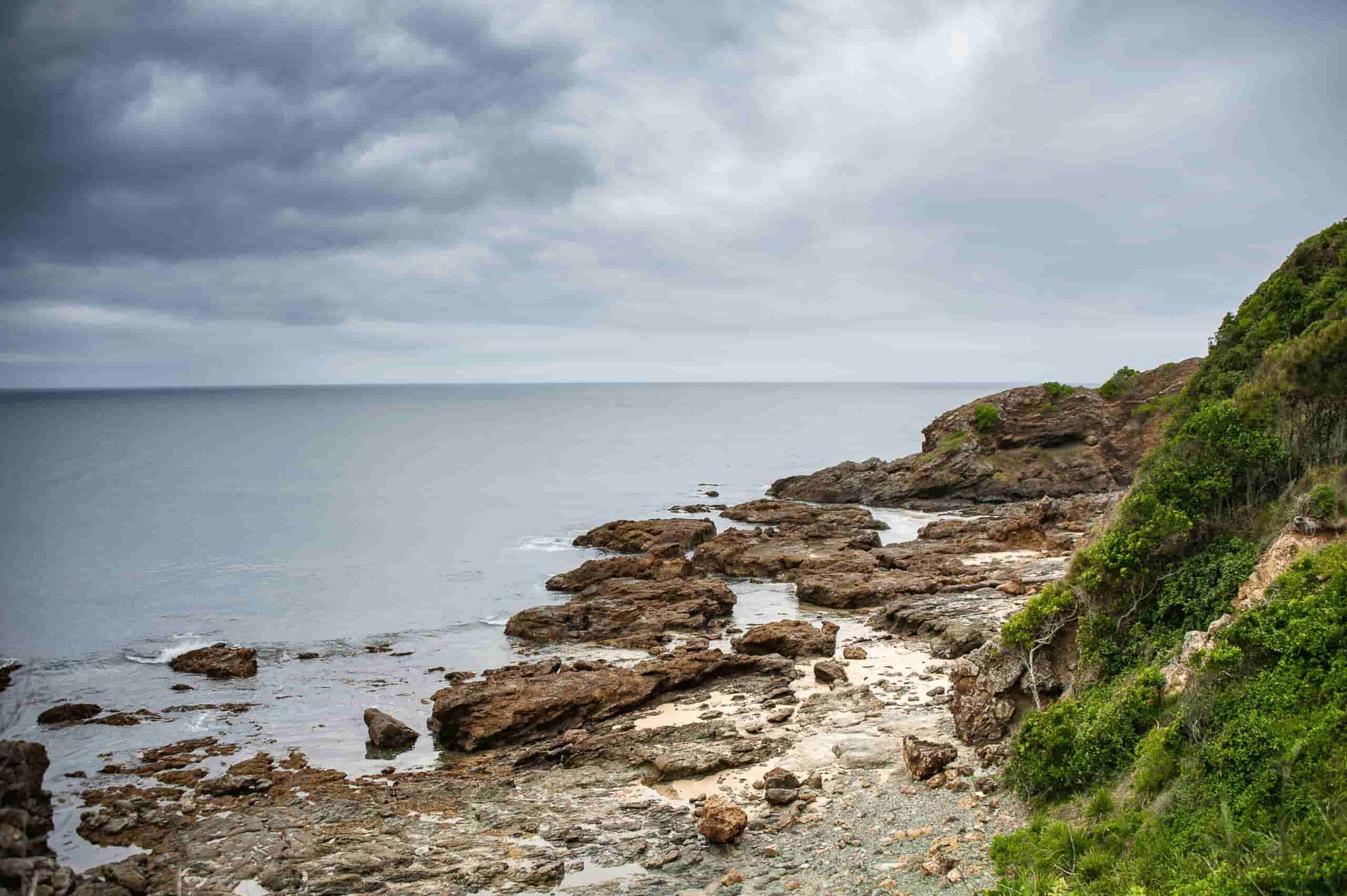 A Rocky Cliff Overlooking the Ocean on a Cloudy Day — Mackie's Concrete Pumping In Hallidays Point, NSW