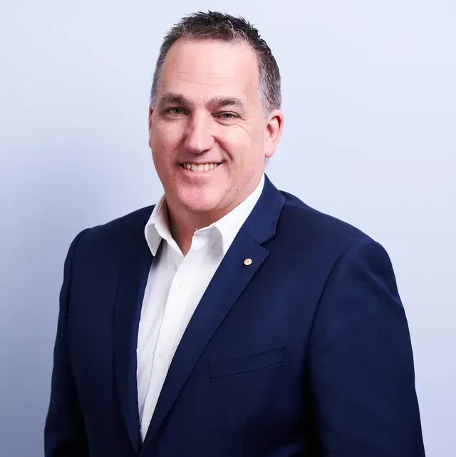 A man in a blue suit and white shirt is smiling for the camera.