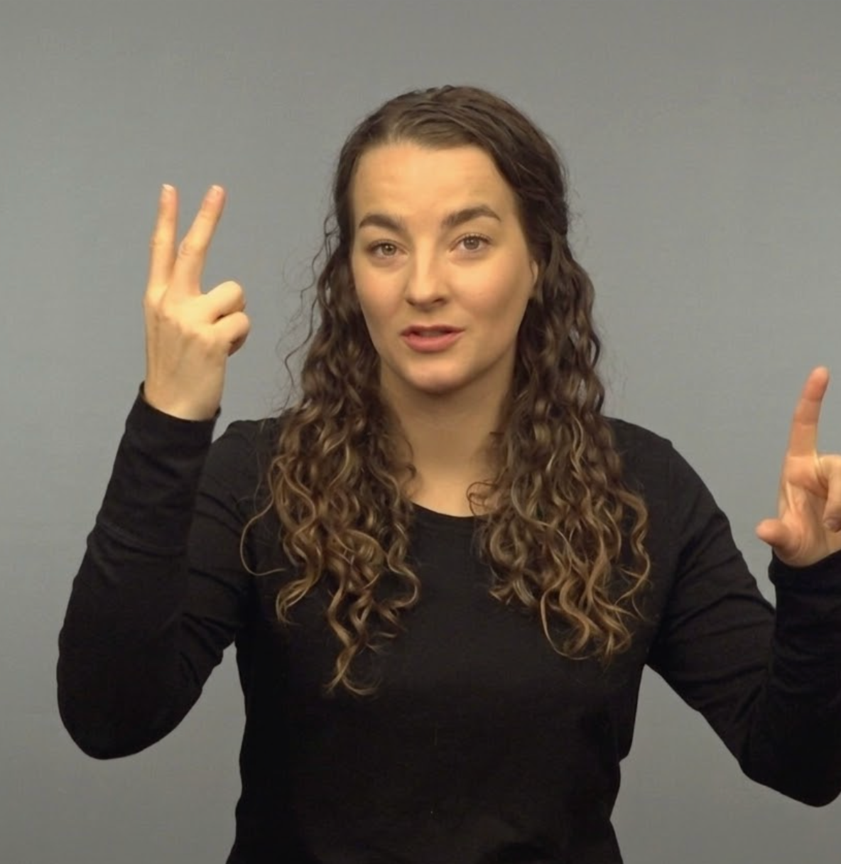 Woman in a black shirt signing with both hands against a gray background
