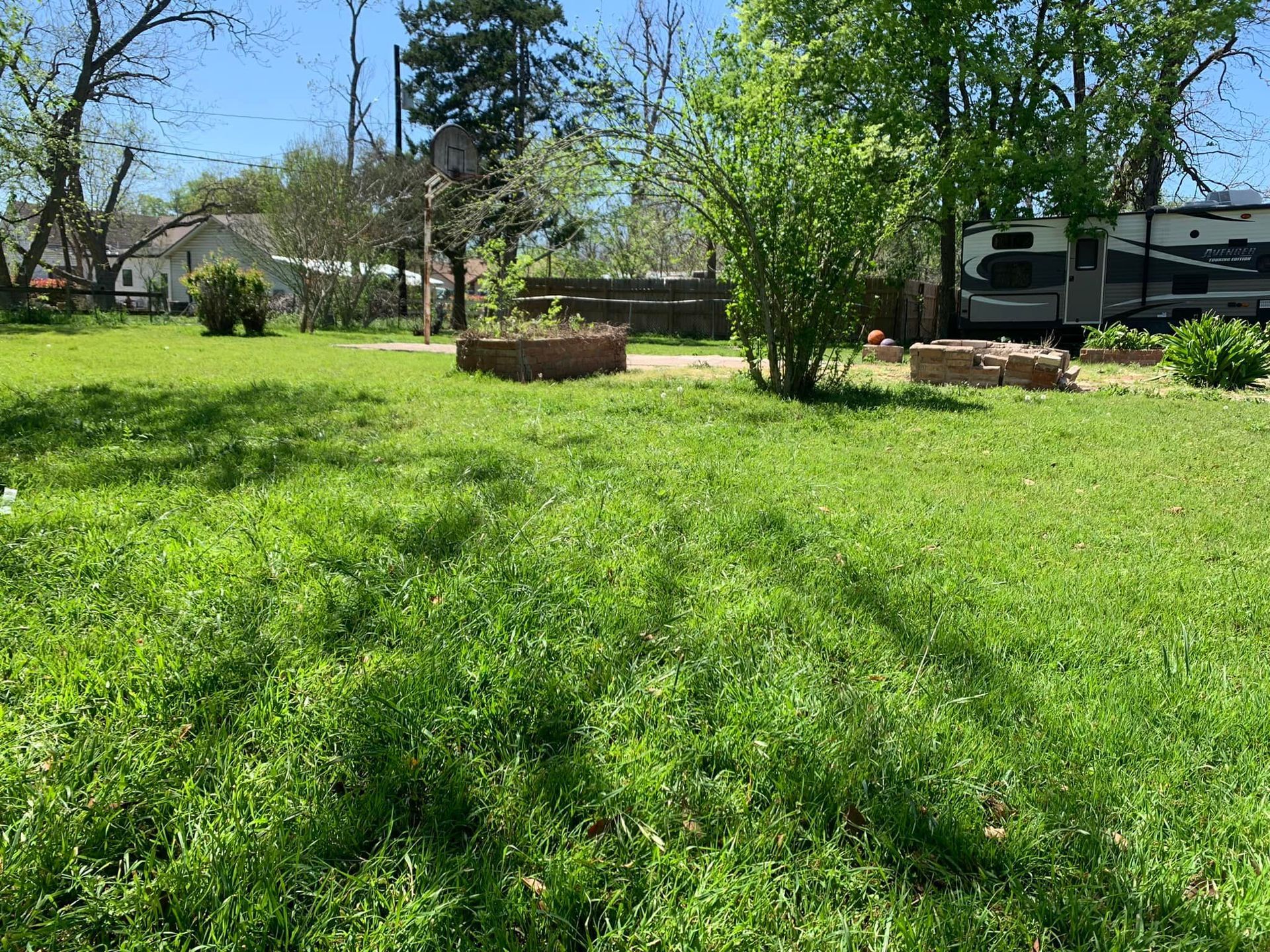 Green grassy yard with a small RV parked in the background. Two raised garden beds in the middle.