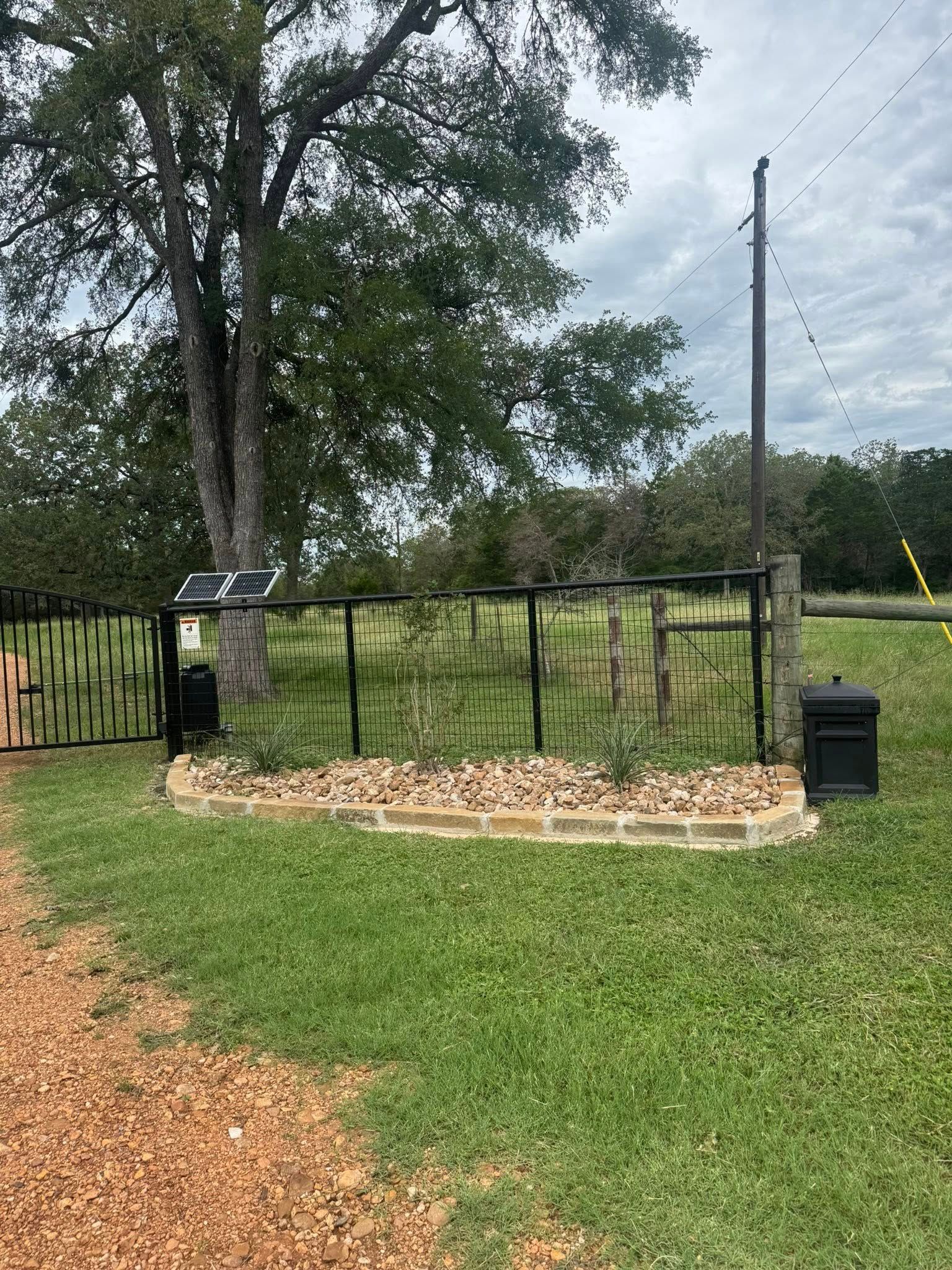 Black metal gate with stone border, in front of a green lawn and tree.