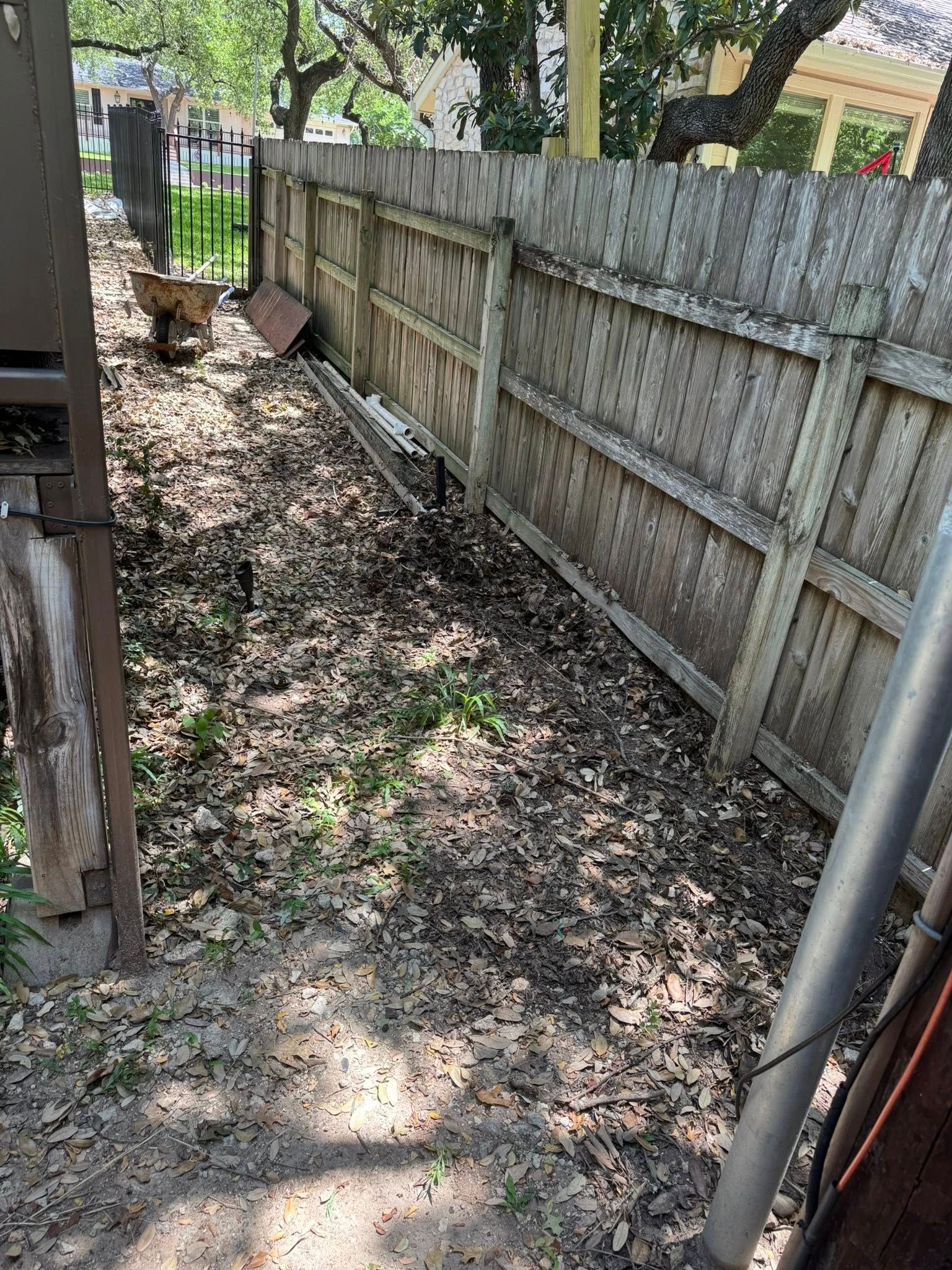 Narrow outdoor pathway covered in leaves, bordered by a wooden fence.
