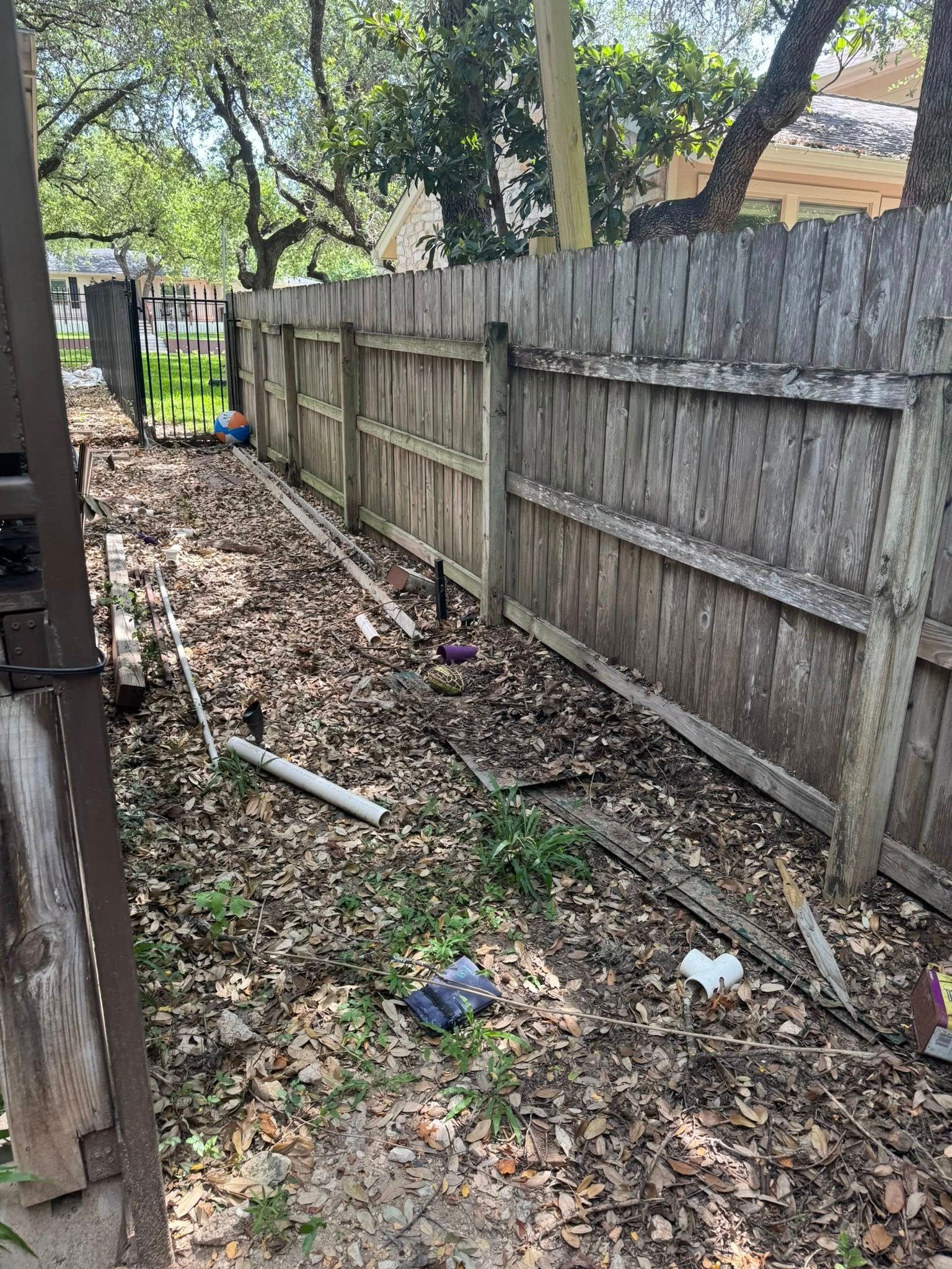 A narrow, debris-filled yard with a weathered wooden fence.