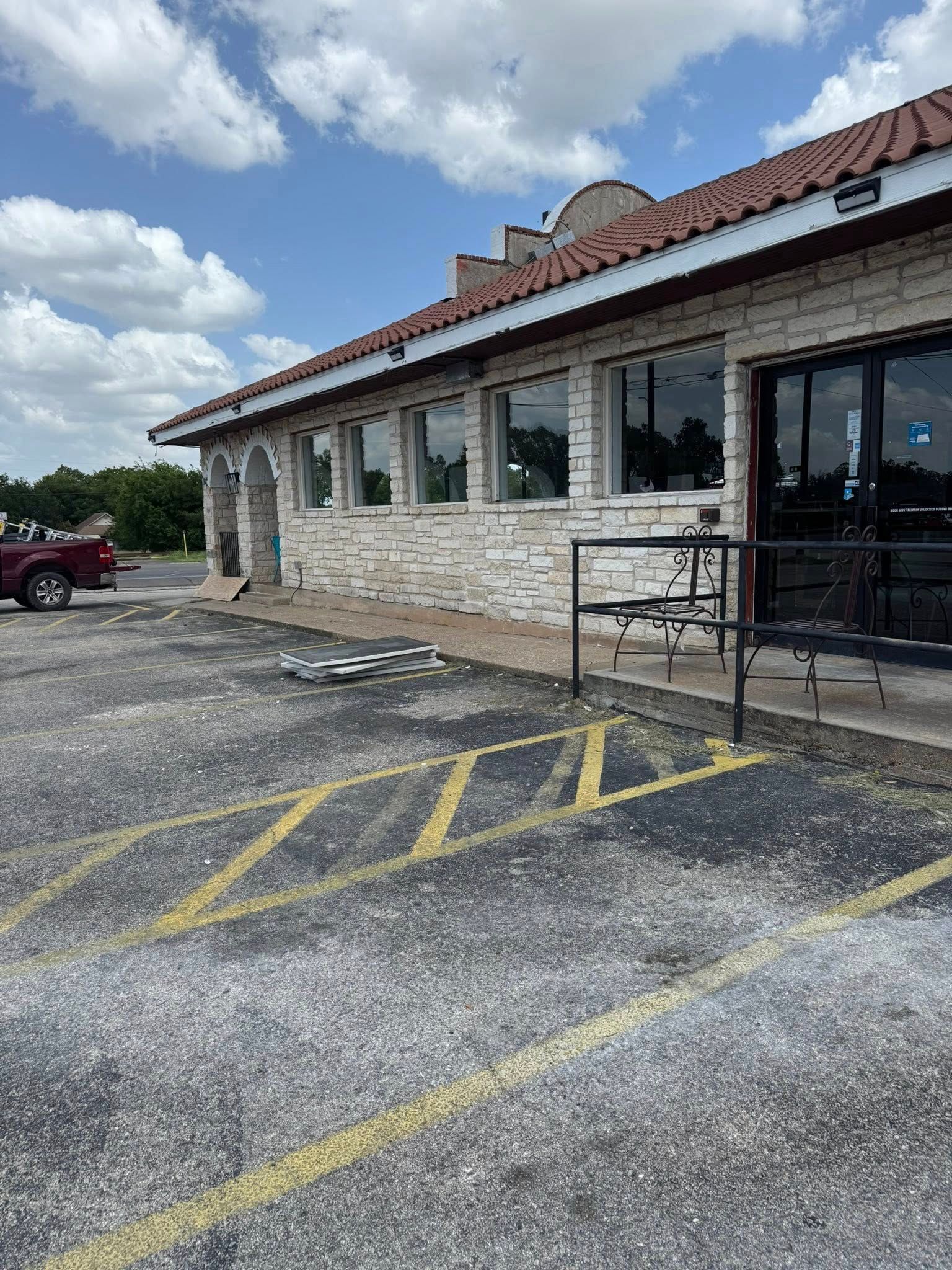 Exterior of a brick building with a tile roof, marked parking spaces, and a red truck nearby.