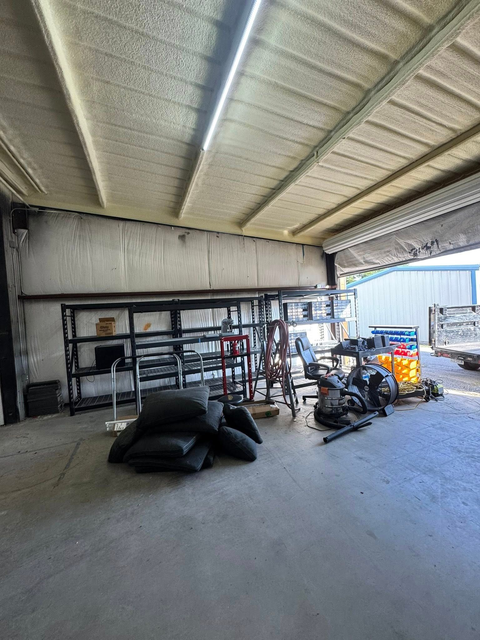 A cluttered storage area under a white-paneled ceiling with metal shelving and various tools.