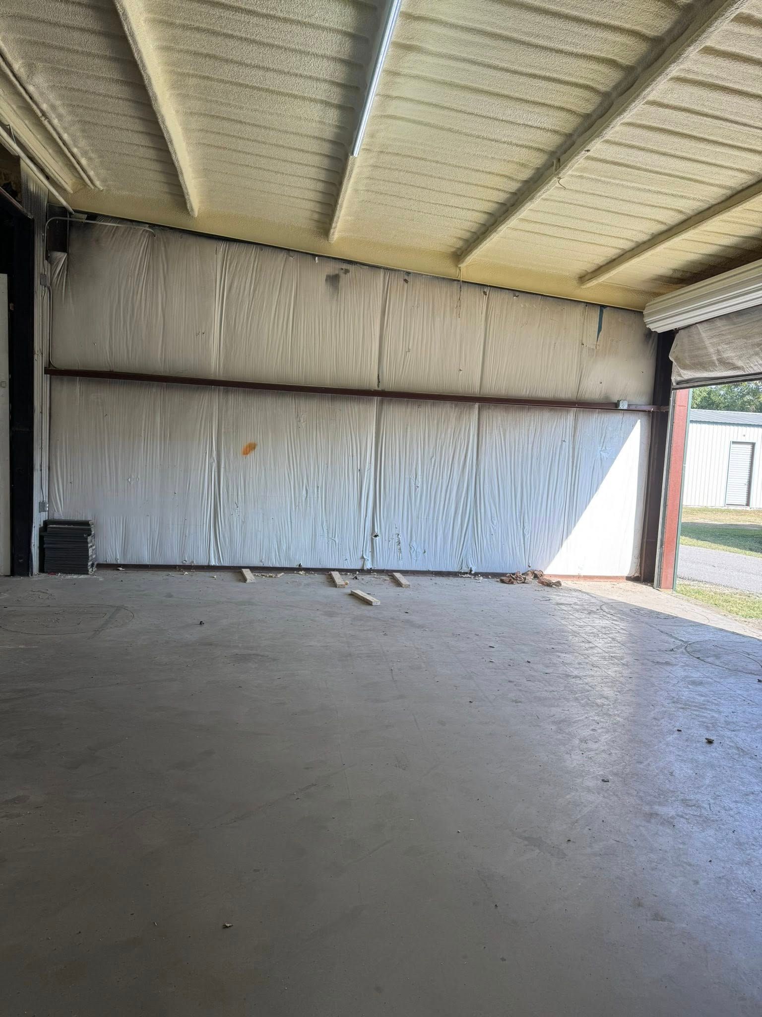 Concrete floored, open-air structure. White walls, foam ceiling, sunlight streams through an opening.