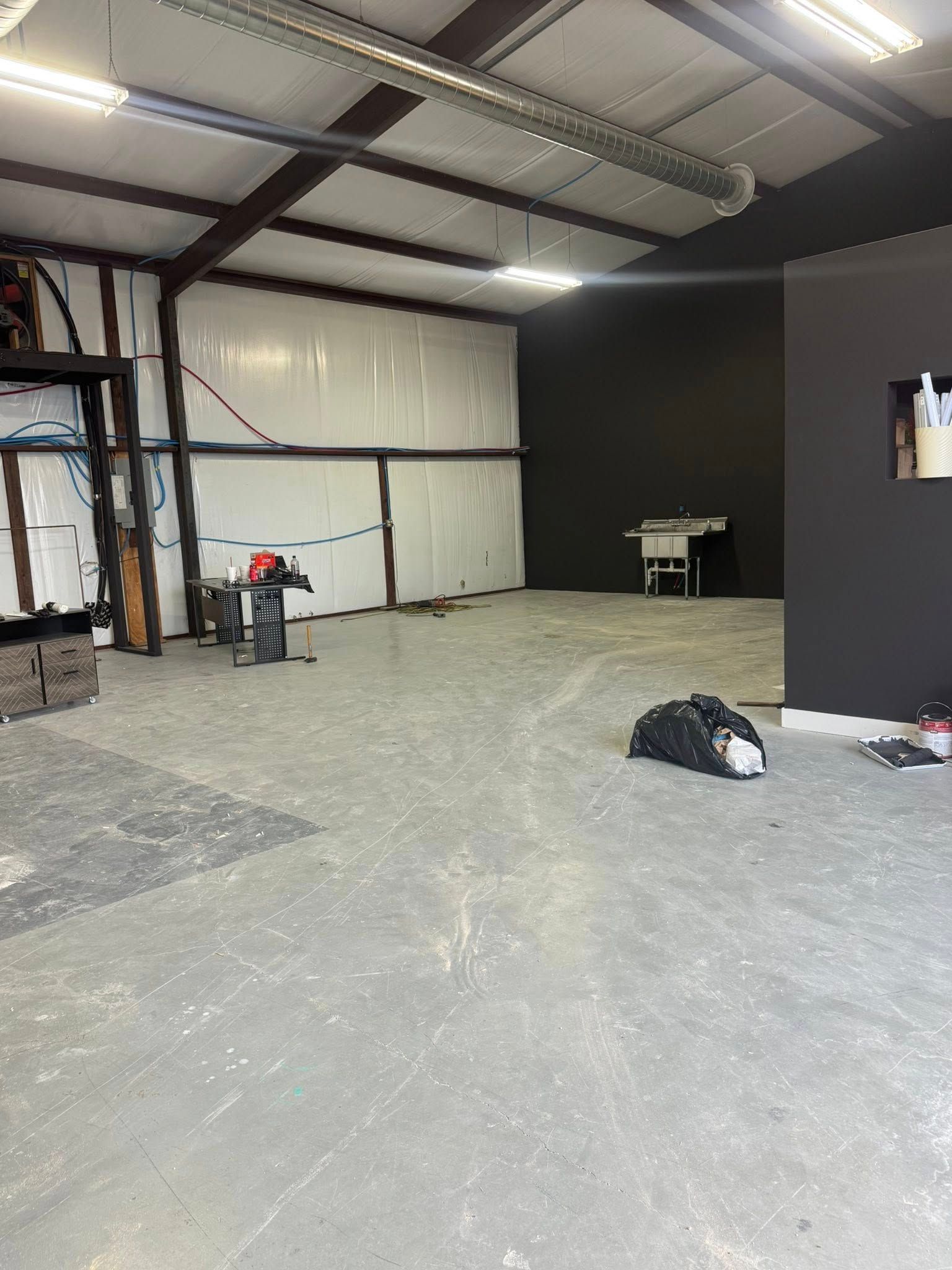 Empty workshop space with gray concrete floor, white walls, and dark gray wall in the back.