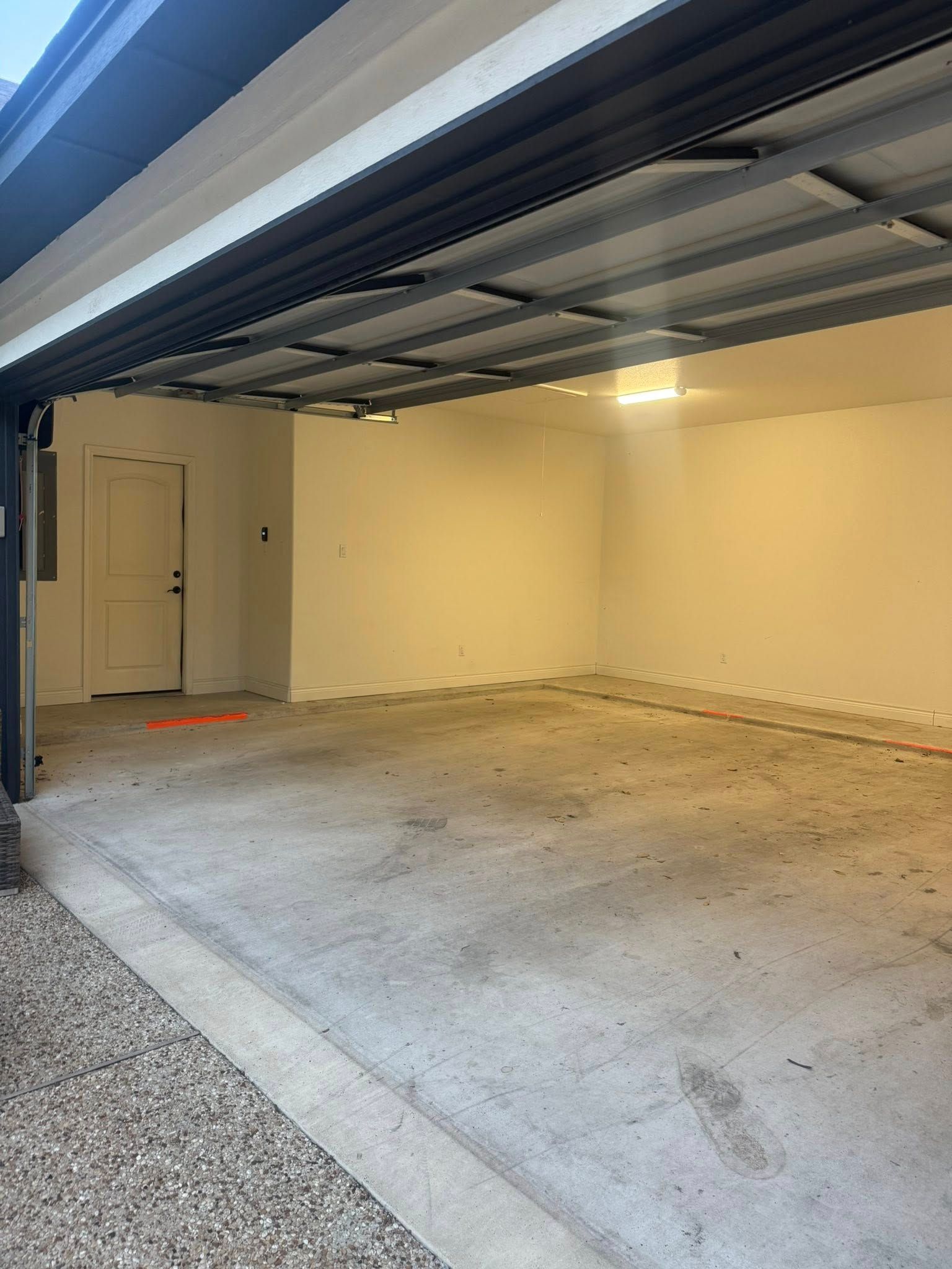 Open garage interior with a concrete floor, white walls, and a door on the far side.
