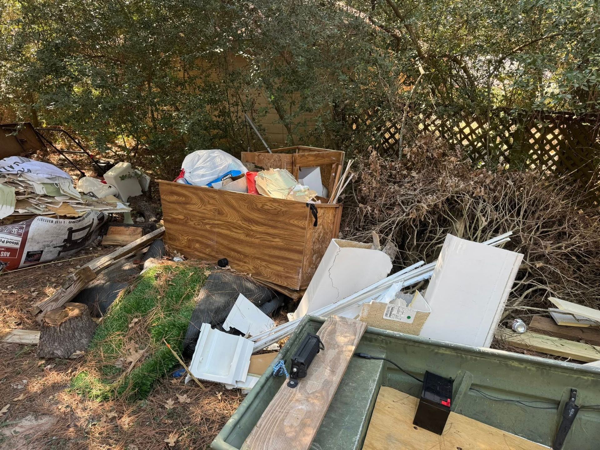 Pile of debris in a wooded area, including wood, drywall, and trash.