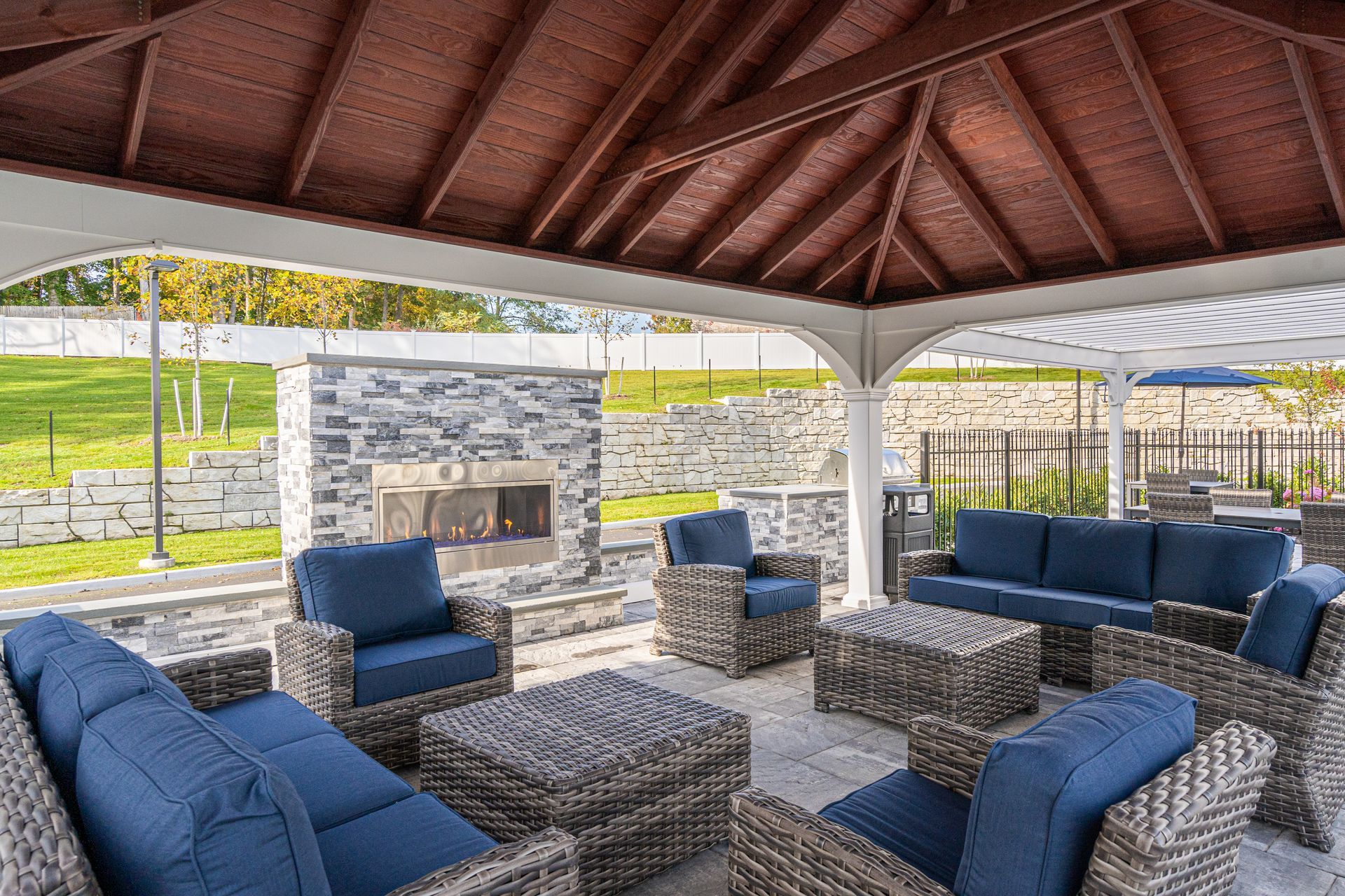 Outdoor seating area with blue cushions, fireplace, and wooden gazebo roof.