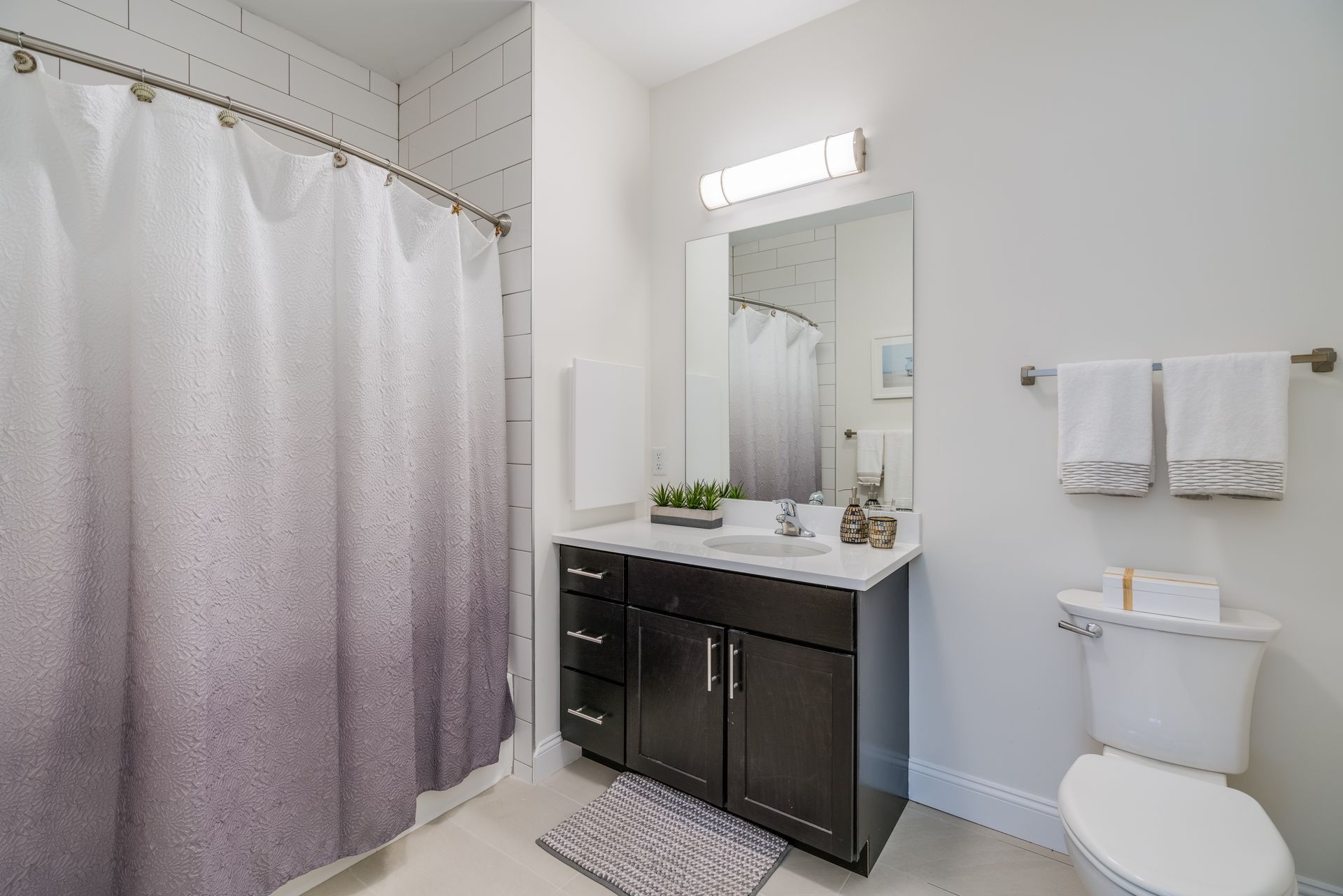 Bathroom with white walls, dark vanity, and a shower curtain with a gradient purple design.