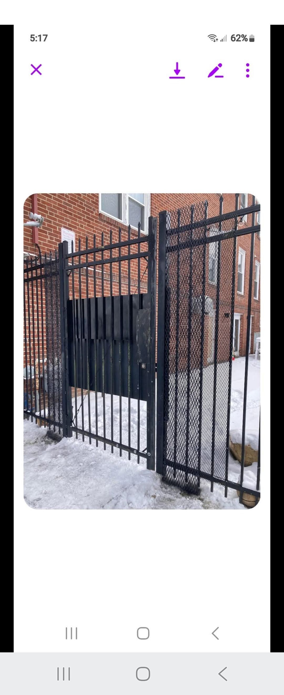 Black metal gate in front of a brick building. Snow on the ground.