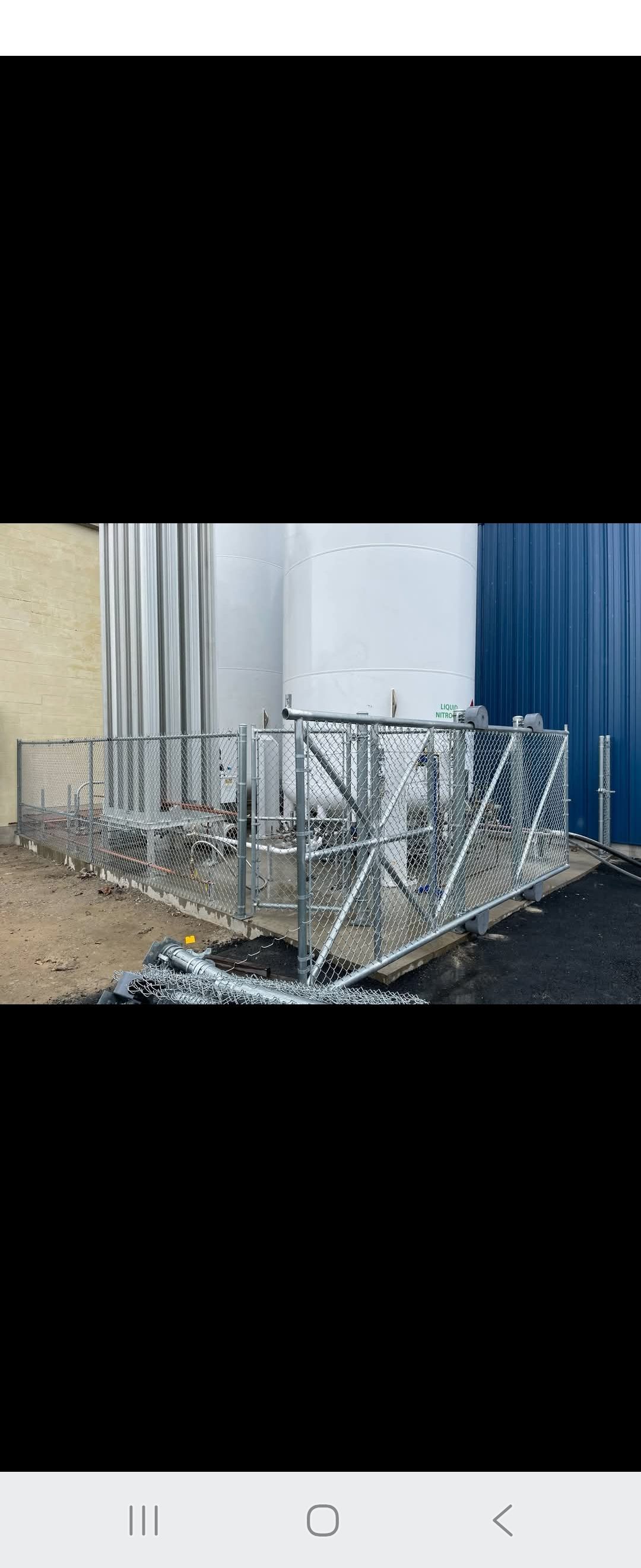 Metal fencing and supports on the ground near industrial tanks and a blue wall.