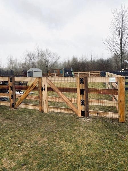 Wooden gate and fence with wire mesh in a grassy field.