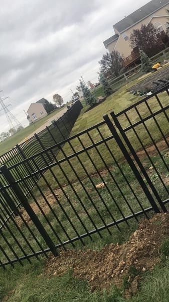 Black metal fence surrounding a grassy yard with houses and power lines in the background under a cloudy sky.