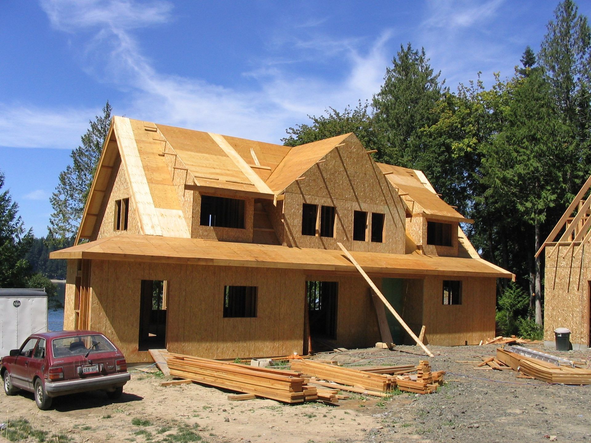A red car is parked in front of a house under construction