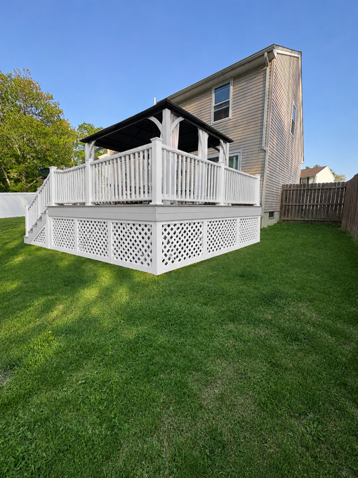 White wooden deck attached to a house, with a lattice base and green lawn in the yard.