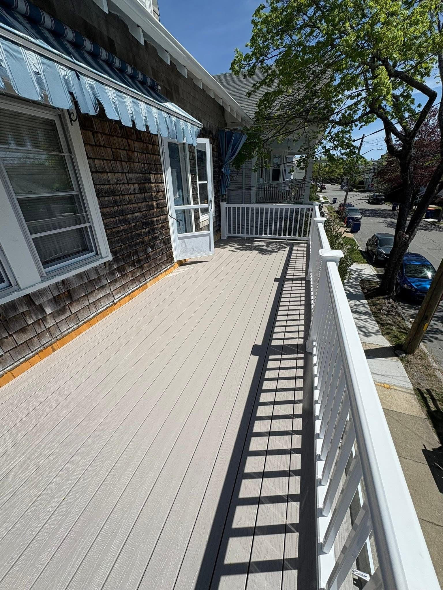 Sunlit apartment balcony with white railing, brick wall, striped awning, and street view below