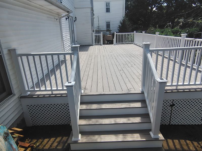 White wooden deck stairs leading to a fenced backyard patio beside a house