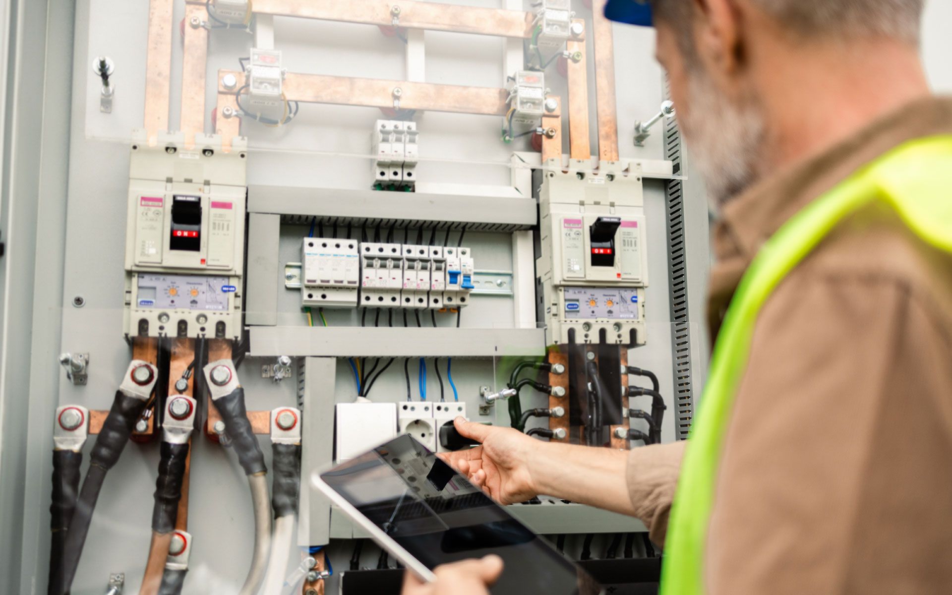 A man is using a tablet to look at an electrical panel.