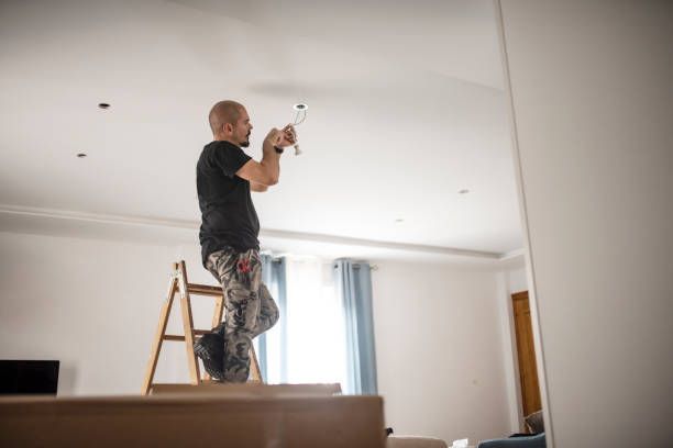 Residential electrician drilling holes in plasterboard installing wiring during home renovation.