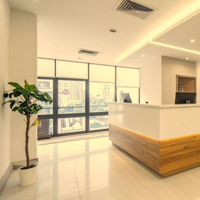 Modern office reception area with a white desk, wooden accents, and a large window overlooking a city.
